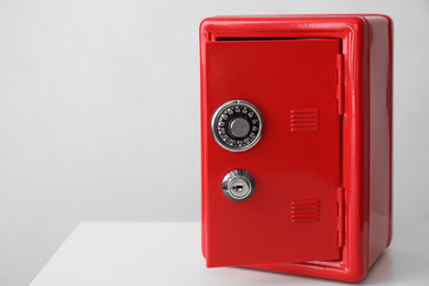 Photo of Red steel safe on white table against light background. Space for text