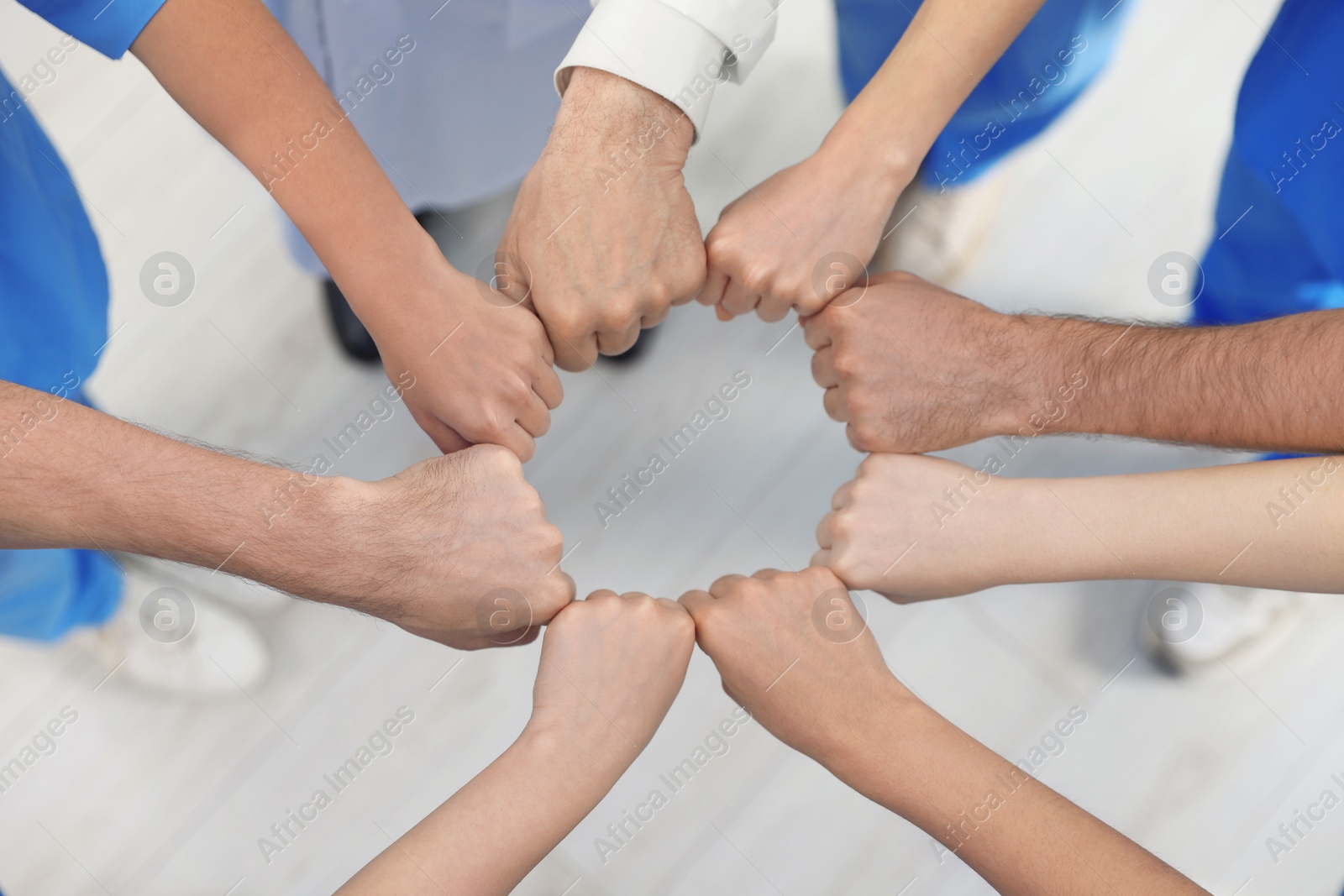 Photo of Doctor and interns holding fists together indoors, above view