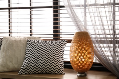 Photo of Pillows and lamp on windowsill in room. Stylish interior elements