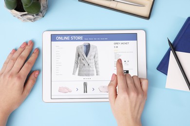 Woman with tablet shopping online on light blue background, top view