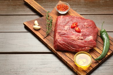 Photo of Fresh raw beef cut, spices and oil on wooden table. Space for text