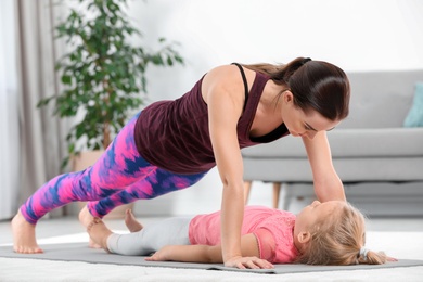 Sportive woman doing fitness exercises with daughter at home