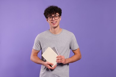 Handsome young man with books on violet background