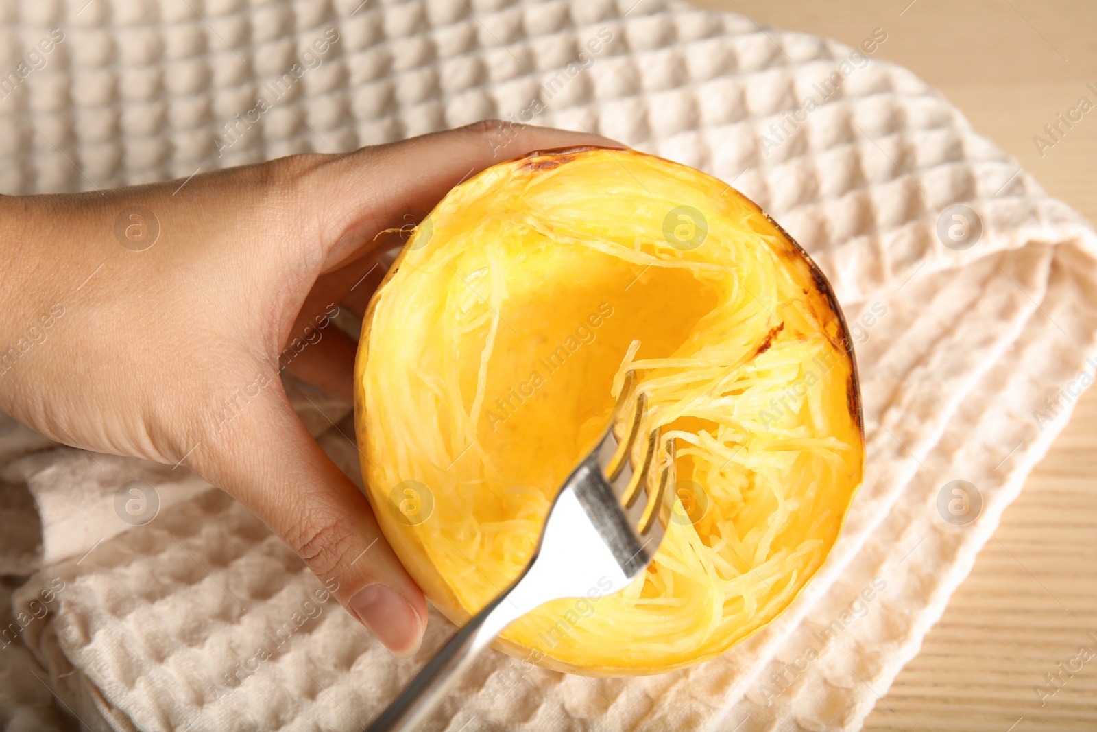 Photo of Woman scraping flesh of cooked spaghetti squash with fork on table, top view