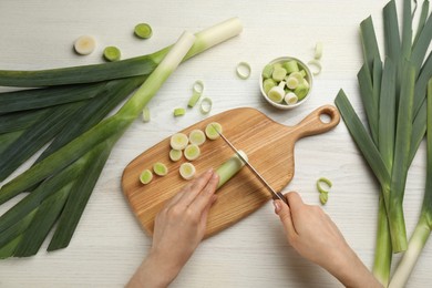 Photo of Woman cutting leek at white wooden table, top view