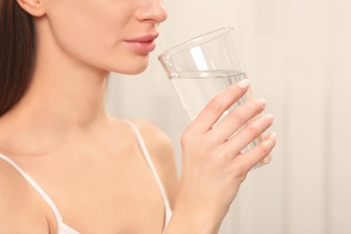 Photo of Healthy habit. Woman drinking fresh water from glass indoors, closeup