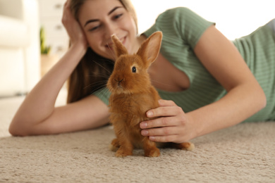 Photo of Young woman with adorable rabbit on floor indoors. Lovely pet