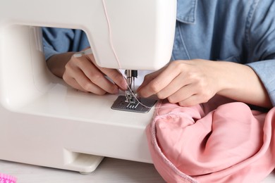 Photo of Seamstress working with sewing machine at white table indoors, closeup