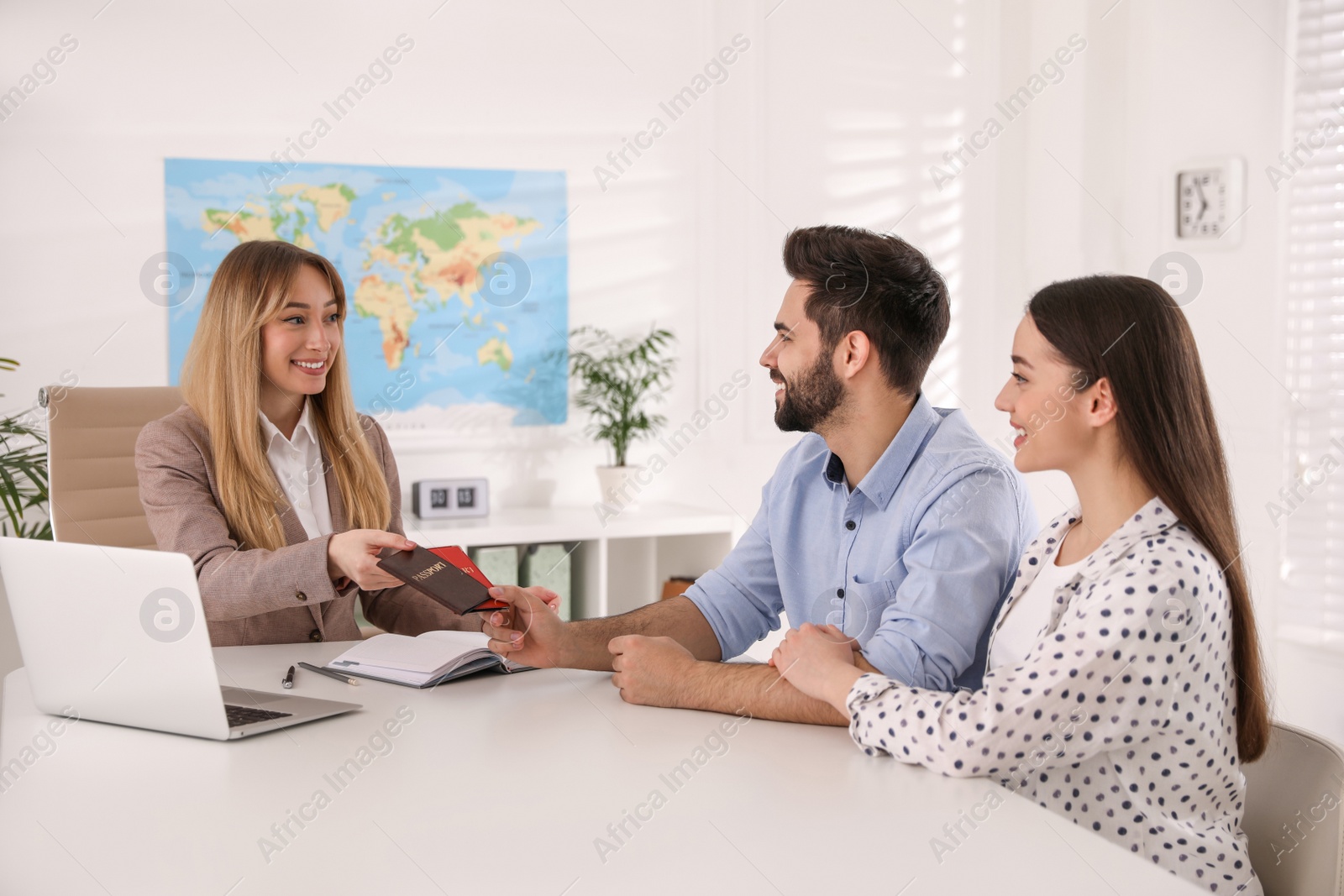 Photo of Manager giving passports to couple at desk in travel agency