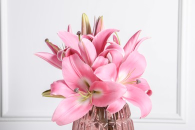 Photo of Beautiful pink lily flowers in vase against white wall, closeup