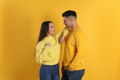Happy couple wearing warm sweaters on yellow background
