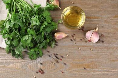 Bunch of raw parsley, oil, garlic and peppercorns on wooden table, flat lay