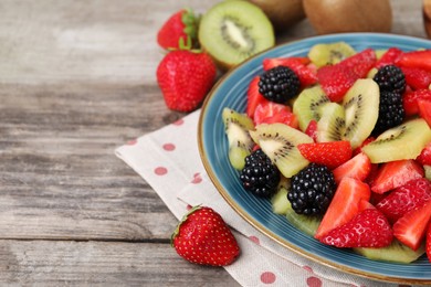 Photo of Plate of delicious fresh fruit salad on wooden table, closeup. Space for text