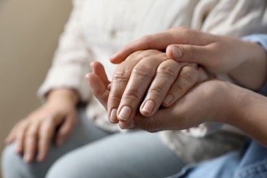 Photo of Woman holding hands with her mother on beige background, closeup. Space for text