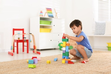 Photo of Cute little boy playing with colorful blocks on floor at home. Educational toy