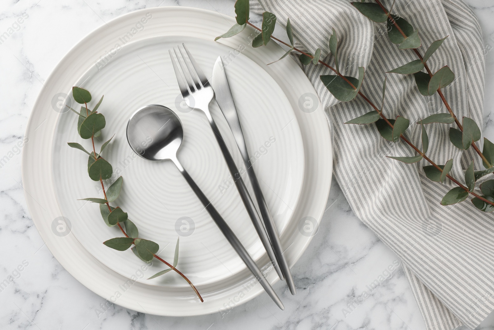 Photo of Stylish setting with cutlery, napkin, eucalyptus branches and plates on white marble table, top view