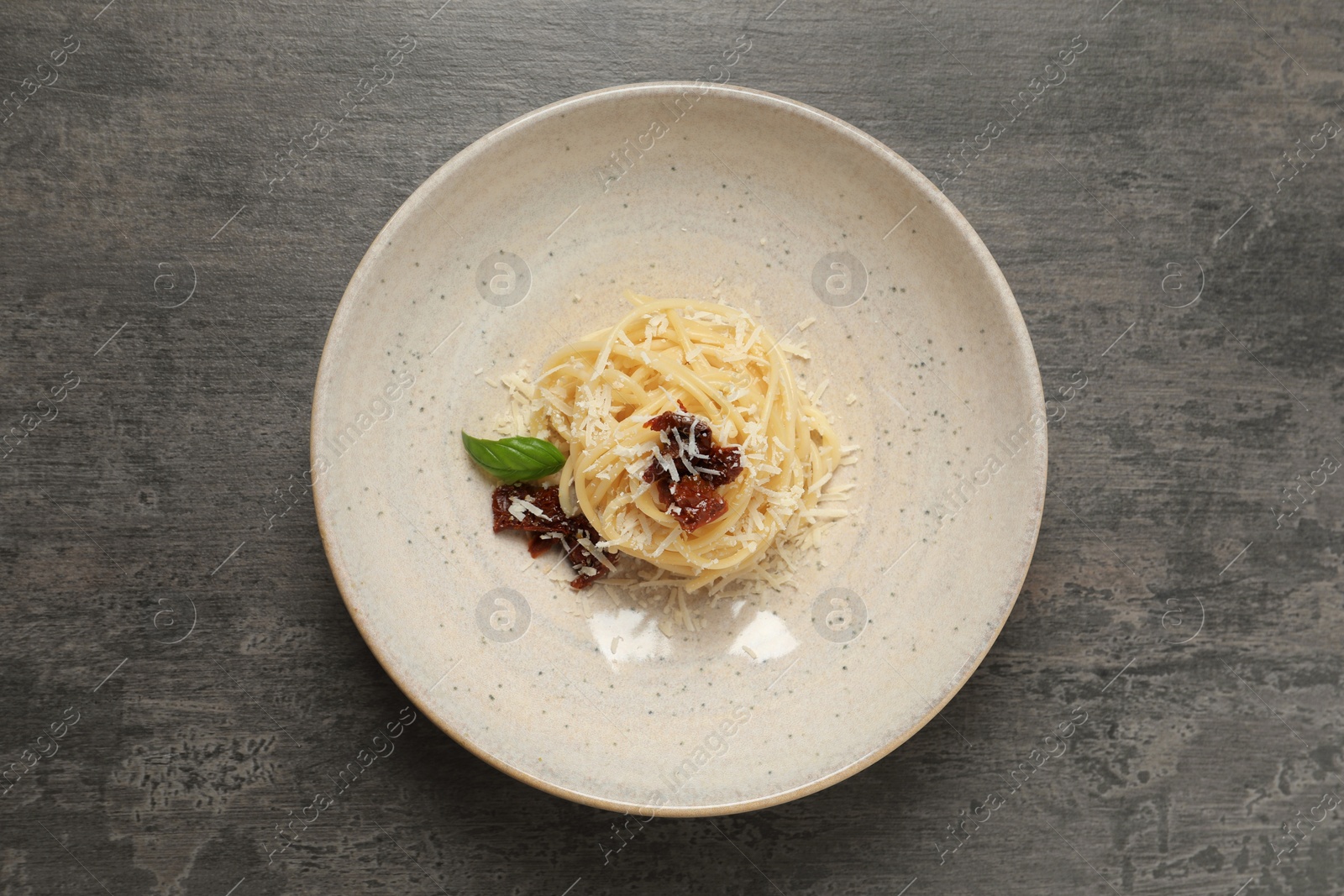 Photo of Tasty spaghetti with sun-dried tomatoes and parmesan cheese on grey table, top view. Exquisite presentation of pasta dish