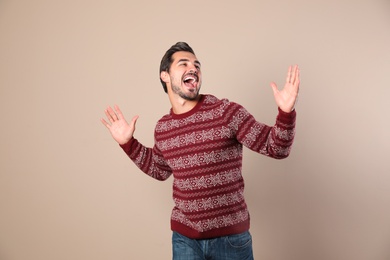 Happy young man in Christmas sweater on beige background