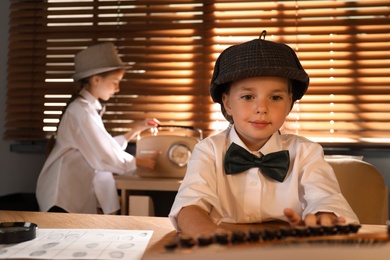 Cute little detective using typewriter while her colleague switching on radio in office