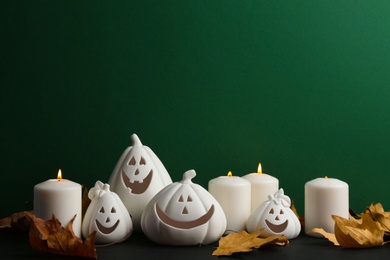 Photo of Composition with pumpkin shaped candle holders on black table against green background, space for text. Halloween decoration