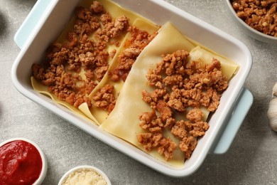 Photo of Cooking lasagna. Pasta sheets and minced meat in baking tray on light textured table, flat lay