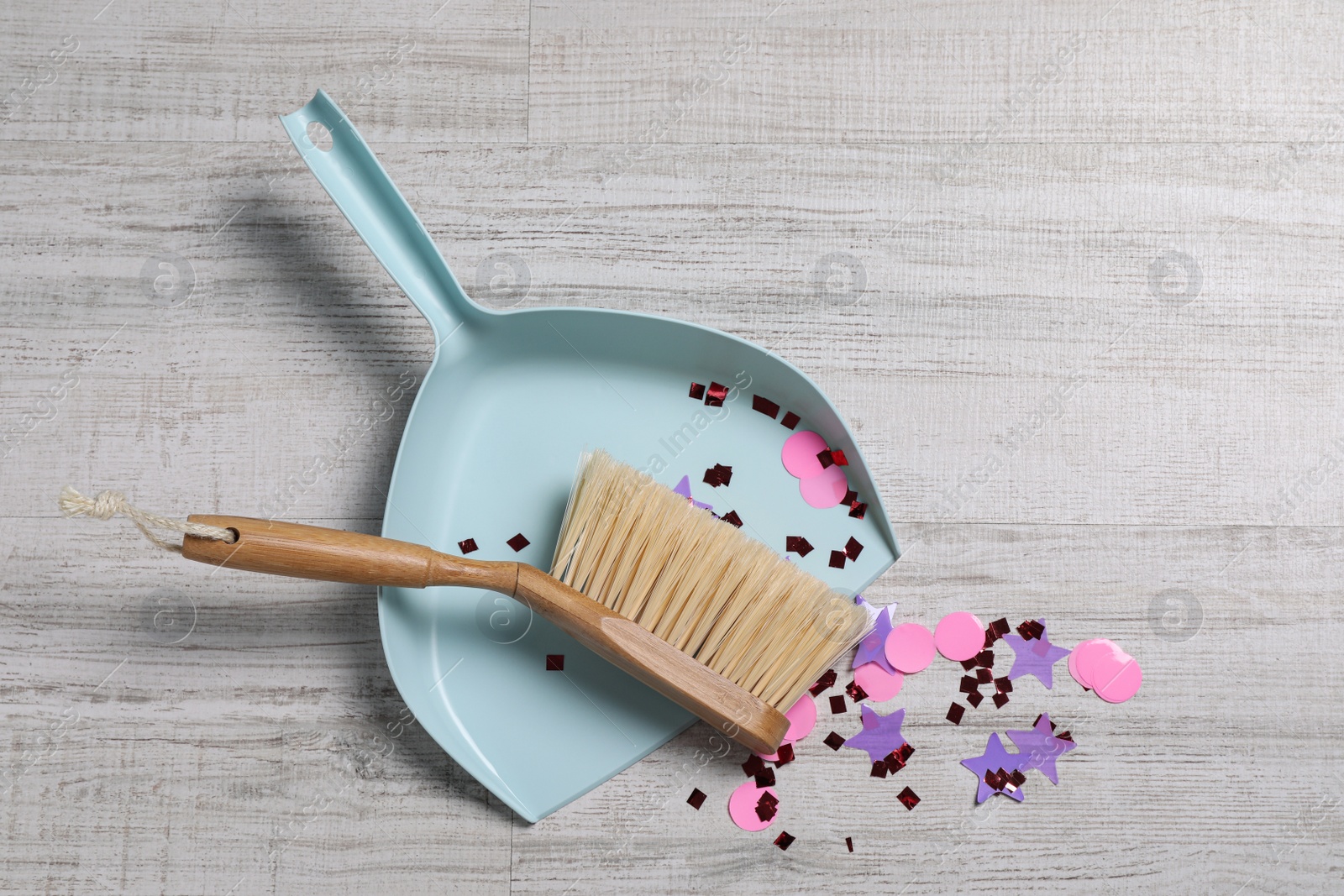 Photo of Light blue dustpan, wooden brush and bright confetti on floor, top view