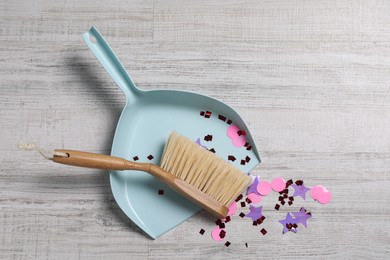 Photo of Light blue dustpan, wooden brush and bright confetti on floor, top view