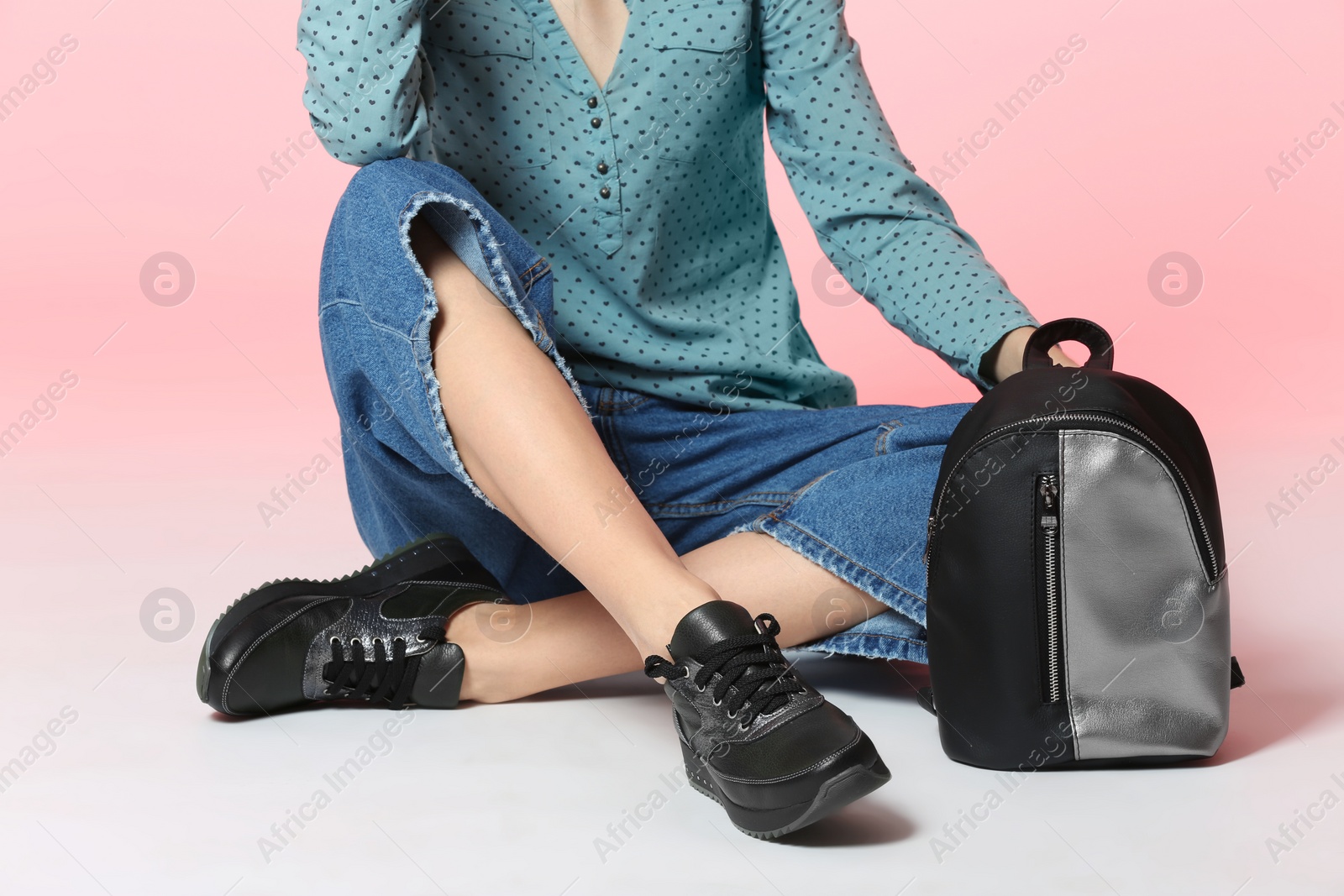 Photo of Fashionable woman in stylish shoes with backpack sitting on color background, closeup