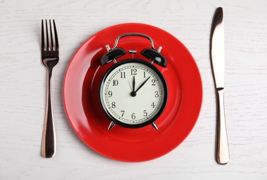 Photo of Alarm clock, plate and cutlery on white wooden table, flat lay. Diet regime