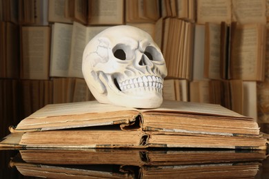 Photo of Human skull and old books on mirror table