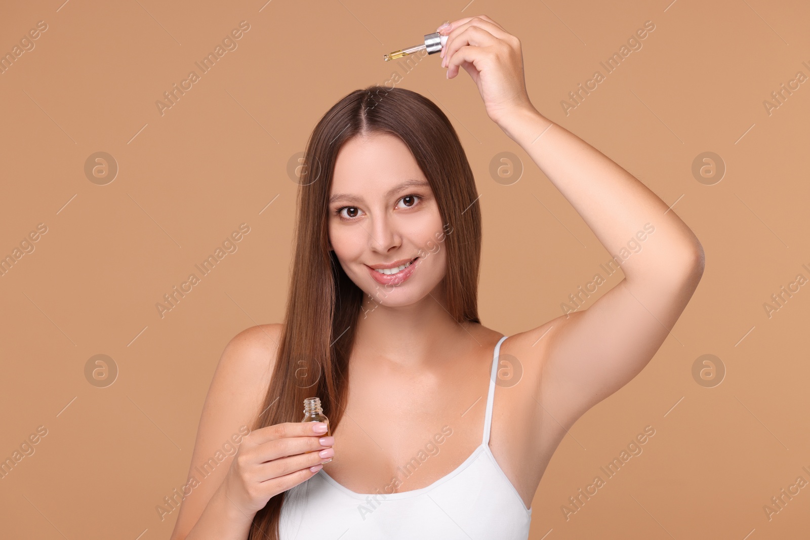 Photo of Beautiful woman applying serum onto hair on beige background