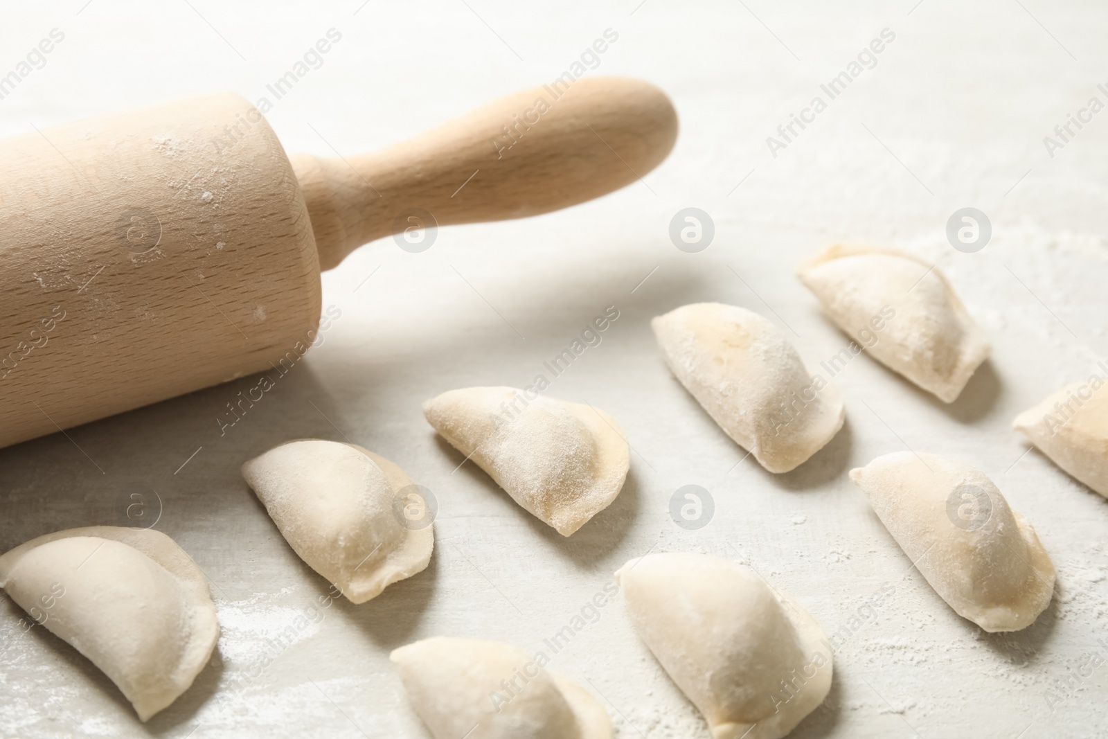 Photo of Raw dumplings and rolling pin on light background, closeup. Process of cooking