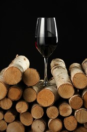 Photo of Red wine in wineglass on wooden logs against black background