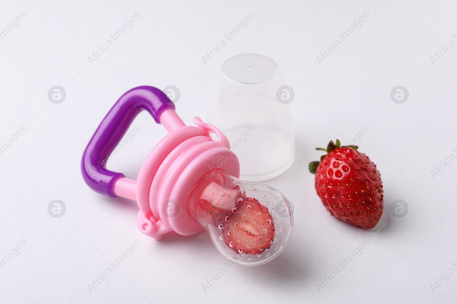 Photo of Nibbler with fresh strawberries on white background. Baby feeder