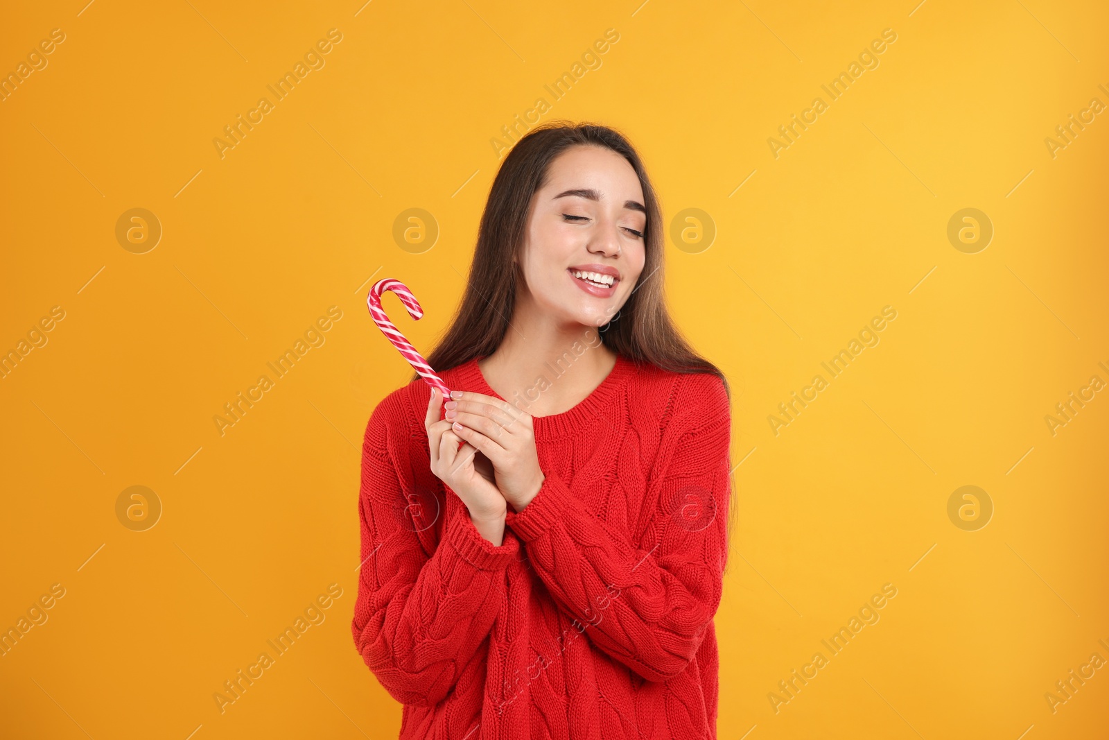 Photo of Young woman in red sweater holding candy cane on yellow background. Celebrating Christmas