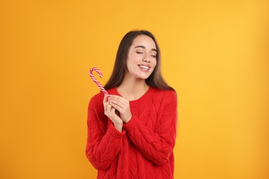 Young woman in red sweater holding candy cane on yellow background. Celebrating Christmas