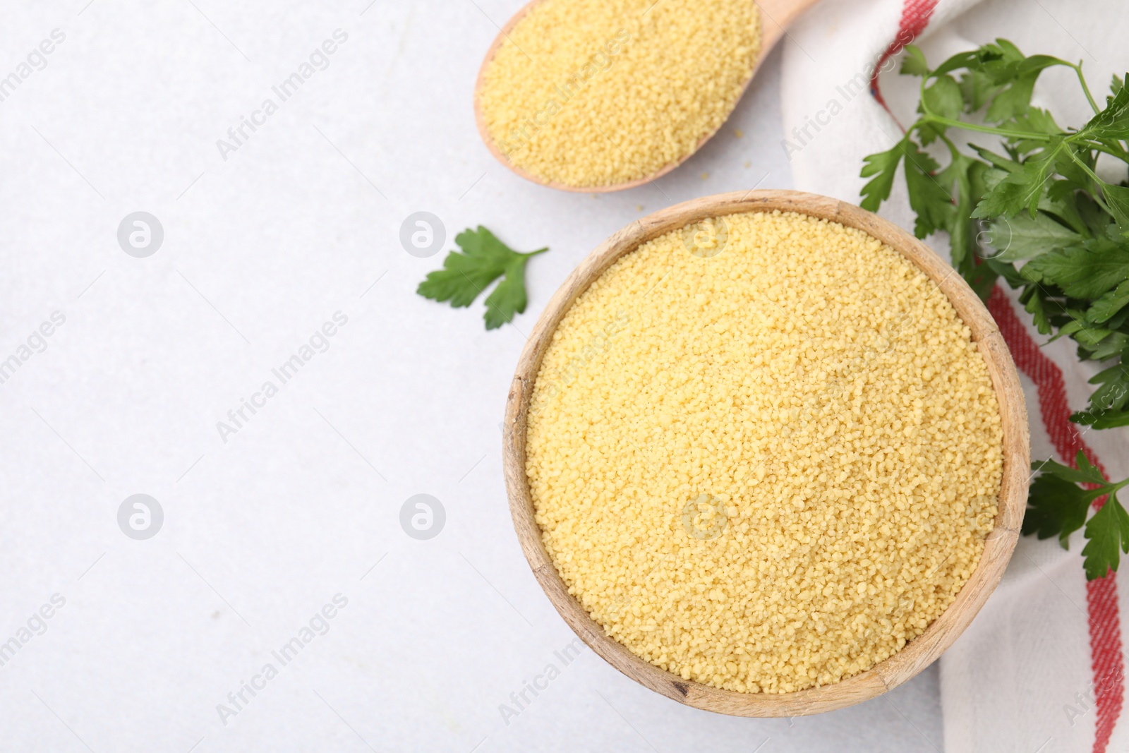 Photo of Raw couscous in bowl, spoon and parsley on light table, flat lay. Space for text