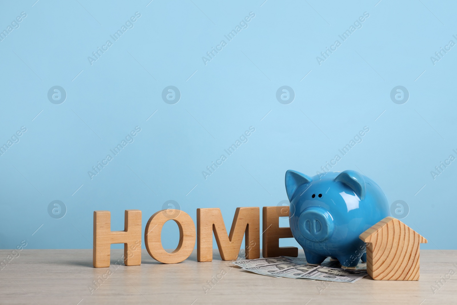 Photo of Piggy bank, house model, banknotes and word Home made of wooden letters on table. Space for text