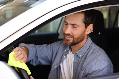 Man cleaning steering wheel with rag in car