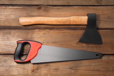 Saw with colorful handle and axe on wooden background, flat lay