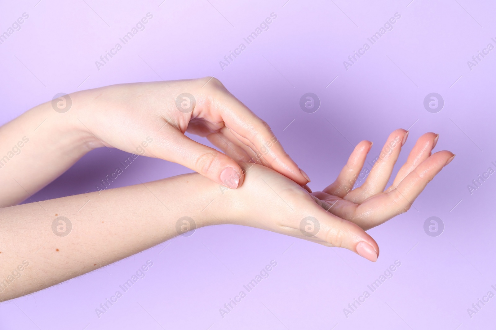 Photo of Woman applying cream on her hand against violet background, closeup