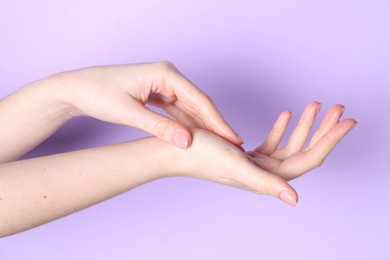 Photo of Woman applying cream on her hand against violet background, closeup