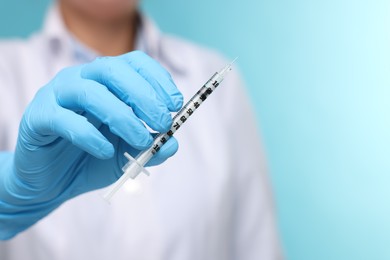 Doctor holding syringe on light blue background, closeup. Space for text