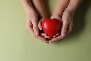 Mother and her child holding red decorative heart on light green background, top view. Space for text