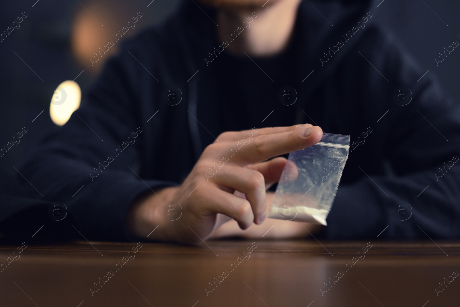 Photo of Criminal holding drug at table indoors, closeup