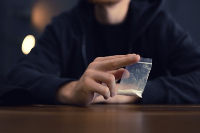 Photo of Criminal holding drug at table indoors, closeup