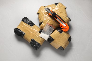 Photo of Packages with narcotics and stationery knife on grey textured table, flat lay
