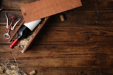 Box with wine bottle, corkscrew and corks on wooden table, flat lay. Space for text