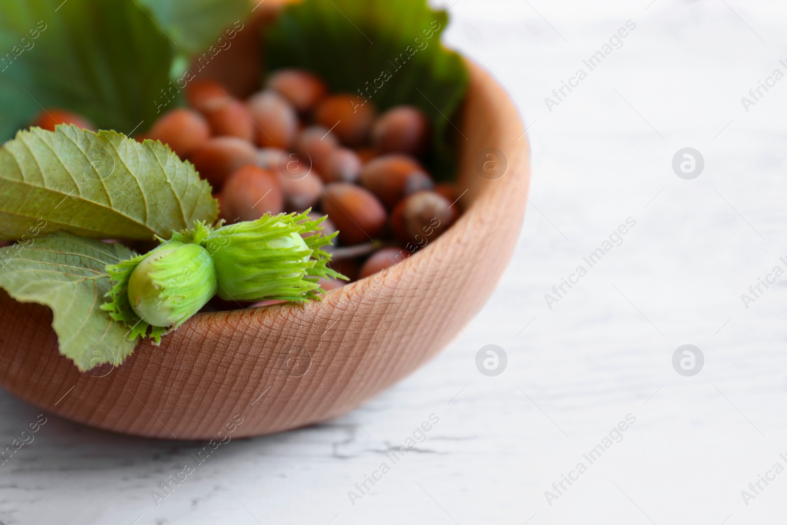 Photo of Bowl with hazelnuts and leaves on white wooden table, closeup. Space for text