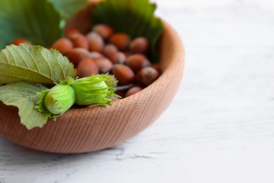 Photo of Bowl with hazelnuts and leaves on white wooden table, closeup. Space for text